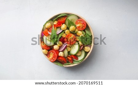 Vegetarian chickpea salad prepared with tomatoes, cucumber, red onion, cress salad and arugula in a paper bowl. Chickpeas are rich in protein and fiber. Zero waste dishware, top view Royalty-Free Stock Photo #2070169511