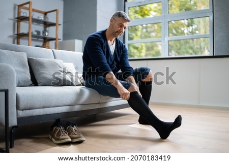 Man Putting On Medical Compression Stockings On Legs Royalty-Free Stock Photo #2070183419