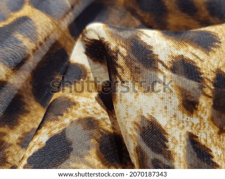 Translucent fabric with leopard print, in folds (macro, texture).