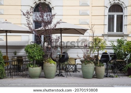 Outdoor terrace or street cafe, bar or restaurant invitingly decorated with green planted pots and modern furniture, bar stools and parasols in front of an old building facade seen in Graz, Austria
