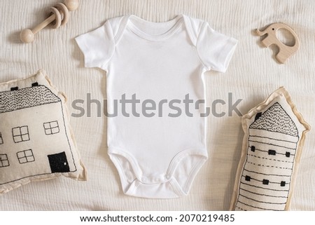 Styled stock photo of clear white baby onesie with scandinavian stitched pillow in the shape of a house and wooden toys on ivory napkin for creating mockup for presentation kids sublimation design