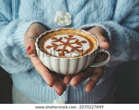 Coffee cup with snowflake sign on frothy surface served in coffee cup holding by female hands with red nail polish. Holidays food art theme for special moments, Merry Christmas and Happy New Year.