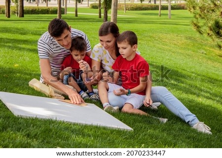 family mom dad and two children sit on green grass in the park hug laugh have fun and and paint a picture together on a beautiful summer warm day