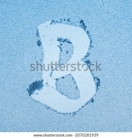 The letter B written on glass with frost in the frost in winter, close up.