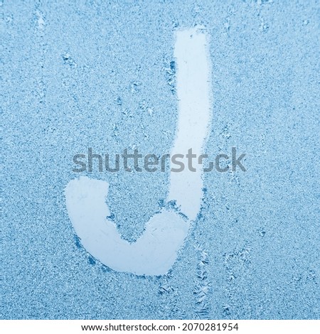 The letter J written on glass with frost in the frost in winter, close up.