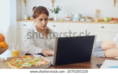 Pretty Woman Sitting at the Kitchen and Work Remotely. Woman Put Her Legs on the Table, on the Table Lying Pizza, Fresh Juice, and Notebooks.Attractive Woman Sitting With Headphones at the Bright Room