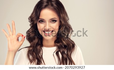  Girl with curly hair  smiling and showing OK sign .Young beautiful blonde woman happy and satisfied. Presenting your product. Expressive facial expressions