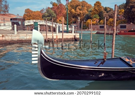 Historic gondola boat in Venice, Italy. Gondola moored near Plazzale Roma in Autumn, with golden and yellow trees and historic bridge behind.