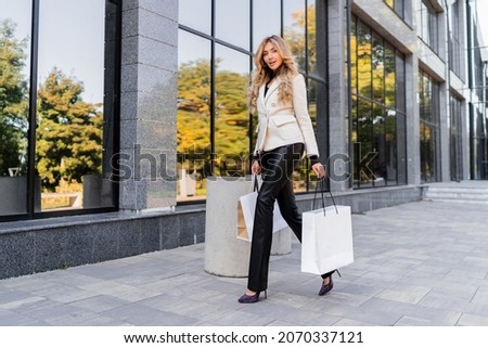 Stunning gracegul blond model holding shopping bags with luxury brends  and posing  outdoor. Urban background.  Royalty-Free Stock Photo #2070337121
