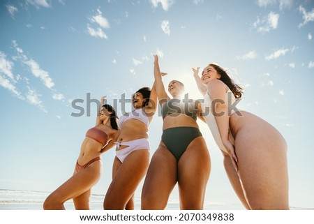 Celebrating spring break. Group of happy female friends cheering with their arms raised while wearing swimwear at the beach. Carefree young women having fun and enjoying their vacation. Royalty-Free Stock Photo #2070349838