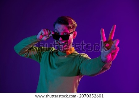 Photo of young excited man happy positive smile show peace cool v-sign isolated over neon color background