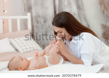 mom kisses babys legs at home in the bedroom. Happy maternity leave time. A mother enjoys spending time with her cute baby, free space