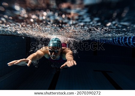 Dark blue water, depth. Underwater view of swimming movements details. One female swimmer in swimming cap and goggles training at pool. Healthy lifestyle, power, energy, sports movement concept. Royalty-Free Stock Photo #2070390272