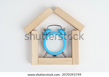 Mockup. On a white background a small house made of wooden planks, inside an alarm clock with empty white space.