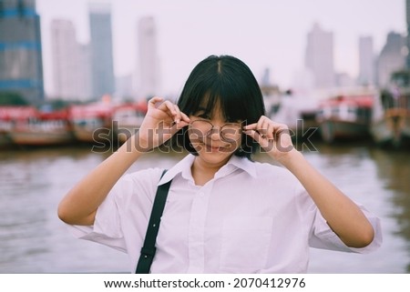 headshot of cheerful asian teenager wearing eyeglasses standing outdoor against city scraper background