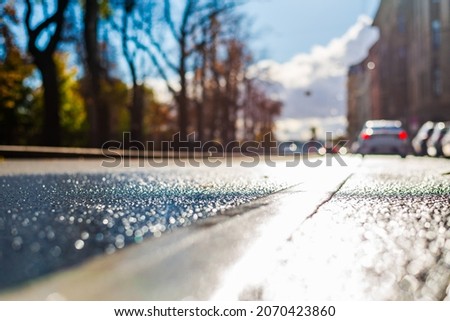 Sunny autumn day. The car drives off along the road. A row of parked cars on the street. The road after the rain. Focus on the asphalt. Close up view from the level of the dividing line.