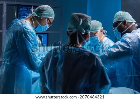 Multiracial team of professional medical surgeons performs the surgical operation in a modern hospital. Doctors are working to save the patient. Medicine, health, cardiology and transplantation. Royalty-Free Stock Photo #2070464321