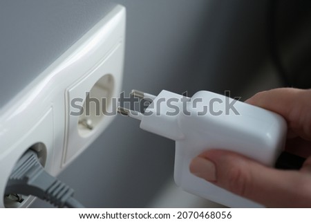 Hands plugging the charger into an outlet in the wall, close-up Royalty-Free Stock Photo #2070468056