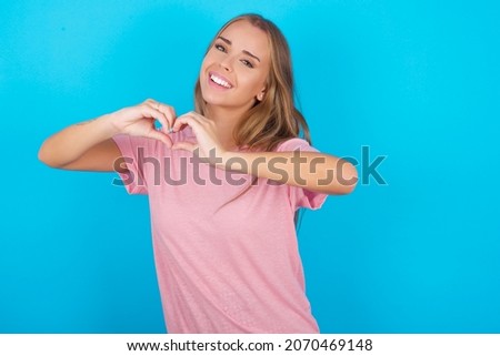 Beautiful caucasian girl wearing pink T-shirt over isolated background smiling in love doing heart symbol shape with hands. Romantic concept.