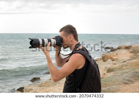A photographer with a backpack on the cliff taking pictures of the sea