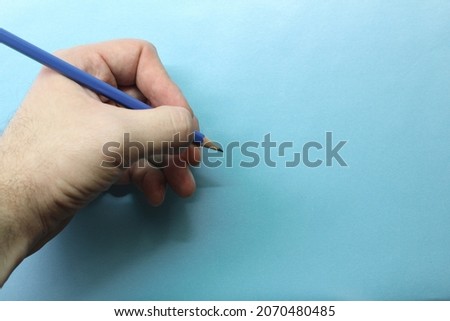 A left hand holding a blue pencil with copy space