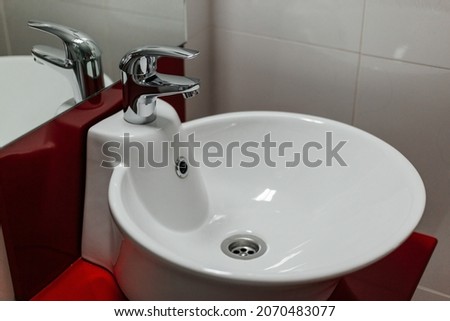 Bathroom interior with round sink and faucet on red stand and white tile background.