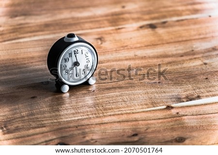 The picture shows a black and white alarm clock on a wooden table or wood background. It's just before 8 a.m.

