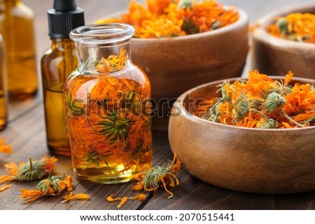 Bottles of calendula essential oil or infusion, wooden bowls and mortar of dried healthy calendula marigold flowers. Alternative herbal medicine. Aromatherapy.