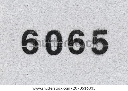 Black Number 6065 on the white wall. Spray paint. Number six thousand sixty five.