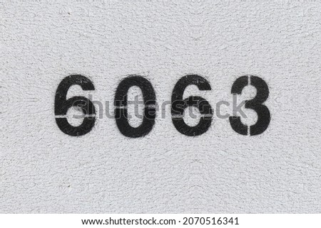 Black Number 6063 on the white wall. Spray paint. Number six thousand sixty three.