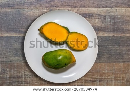 Typical Brazilian fruit mango sword on white plate on rustic wooden background in top view. (Manga espada)
