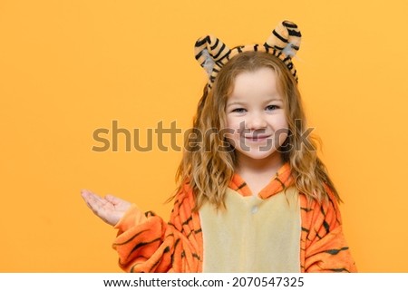 cute smiling girl in tiger costume on isolated yellow background with space for text christmas concept. High quality photo Royalty-Free Stock Photo #2070547325