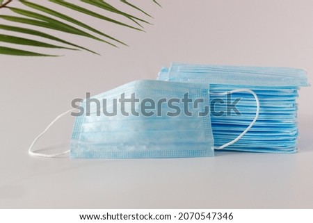 Many new medical facial three-layer masks are stacked and one mask lies next to a light background under a palm tree