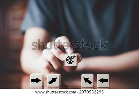 Businessman holding wooden cube with target board icon and arrow on wooden table. Goals and planning for success in marketing business, achieve the objective concept. Closeup and free copy space