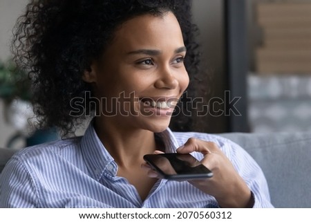Close up smiling African American woman recording audio message or talking, holding smartphone, happy attractive young female chatting online by speakerphone, activating virtual digital assistant