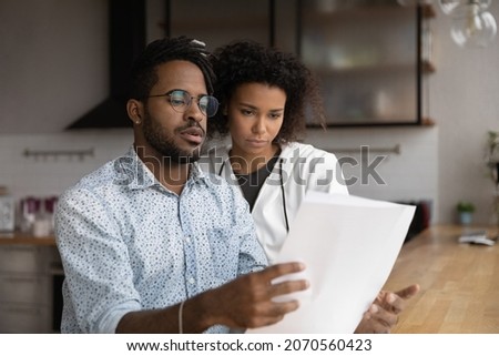 Focused stressed young diverse man woman family couple looking through paper correspondence, feeling dissatisfied reading letter with bad news, bank loan rejection notification or eviction letter. Royalty-Free Stock Photo #2070560423