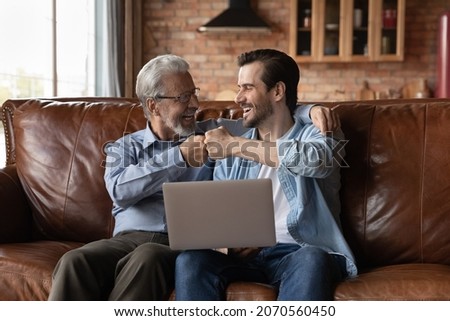That is great. Excited diverse age males senior father young adult son sit on sofa bump fists embrace. Grown grandson old grandfather celebrate soccer team victory after watching sport game on laptop Royalty-Free Stock Photo #2070560450