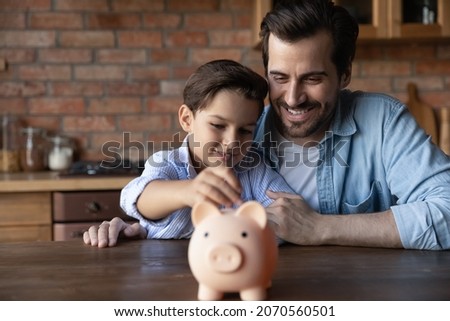ABC of finance. Smiling father support junior school age son in wish to save pin money teach rational economy wise budget planning. Caring dad hug preteen child boy putting pocket change to piggybank Royalty-Free Stock Photo #2070560501