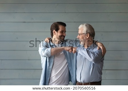 Together we are the power. Bonding mature grandpa young grandson bump fists with smile trust support one another. Happy younger older men relatives friends express unity stand by grey wall. Copy space Royalty-Free Stock Photo #2070560516