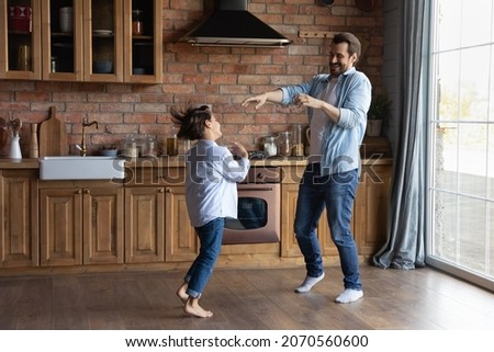 Funny dances. Happy young father little son new cottage house tenants renters dancing on warm wooden floor at cozy kitchen interior. Active foster dad adopted tween kid have fun at home jump by music Royalty-Free Stock Photo #2070560600