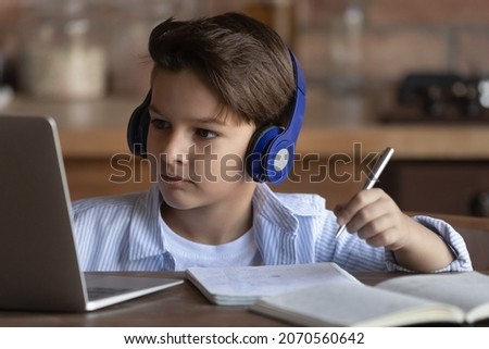 Homeschooling. Focused preteen boy in modern headset study from home look on computer screen take notes to copybook. School age child engaged in learning on distance listen to teacher at online lesson Royalty-Free Stock Photo #2070560642