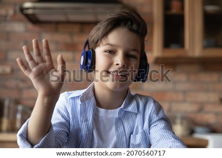 Remote education for children. Screen view portrait of junior school age boy in wireless headphones join online class wave hand greet tutor teacher. Smiling tween kid look at web camera make videocall Royalty-Free Stock Photo #2070560717