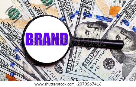 Background with dollar bills under a magnifying glass with the text BRAND. Financial concept