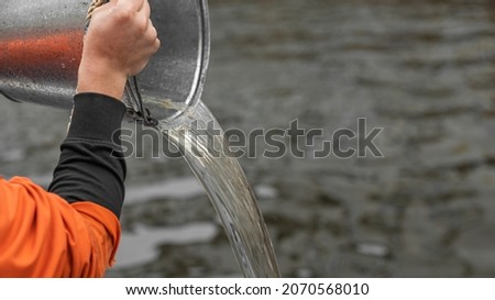 a man pours water out of a bucket. pouring out the liquid. advertising picture. a man's hand holds a galvanized bucket.