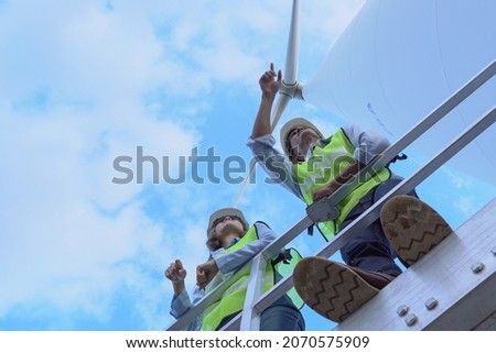 Male and female electric turbine engineers discussing, looking, inspection under turbine tower in the electric turbine farm maintenance operations. Clean energy from nature. Royalty-Free Stock Photo #2070575909