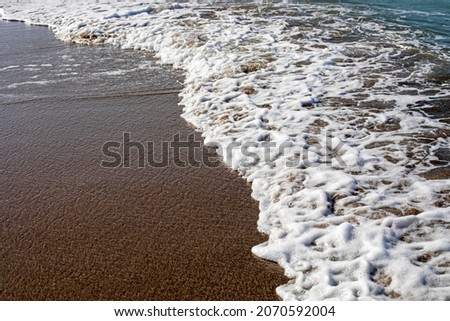 sea background surf with foam on sandy beach top view, horizontal
