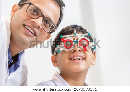 Smiling Indian-thai boy choosing glasses in optics store, Boy doing eye test checking examination with optometrist using trial frame in optical shop Royalty-Free Stock Photo #2070593591