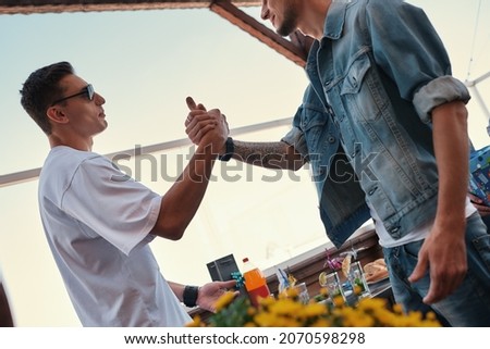 My best friend. Two young and handsome men shaking hands while standing on the roof and enjoying party