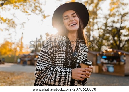attractive young woman walking in autumn street wearing checkered coat, black hat, happy mood, fashion style trend, black friday sale, sunny Royalty-Free Stock Photo #2070618098