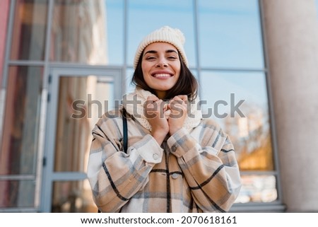 stylish attractive young smiling woman walking in street in winter outfit with coffee wearing checkered coat, white knitted hat and scarf, happy mood, fashion style trend Royalty-Free Stock Photo #2070618161